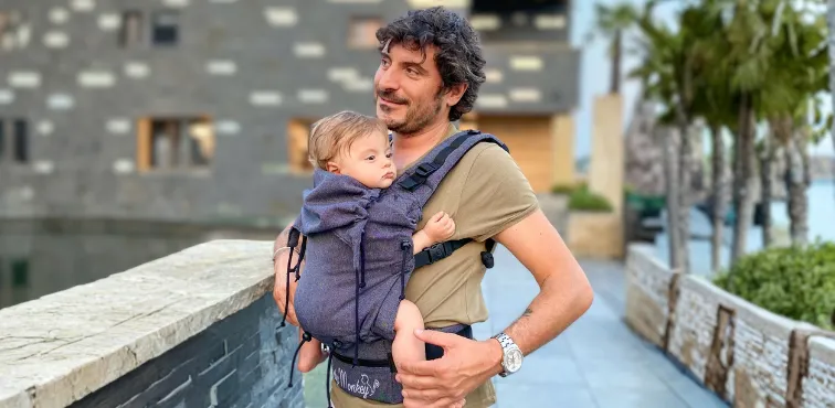 Bambino portato fronte genitore in un marsupio ergonomico